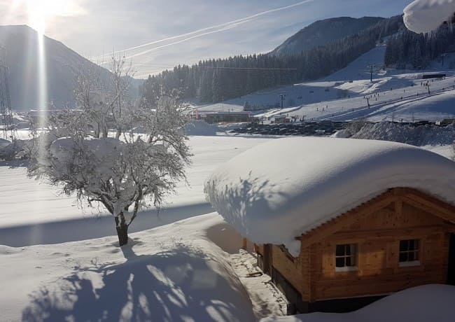Blick auf winterlich verschneite Hütte und die Skipiste